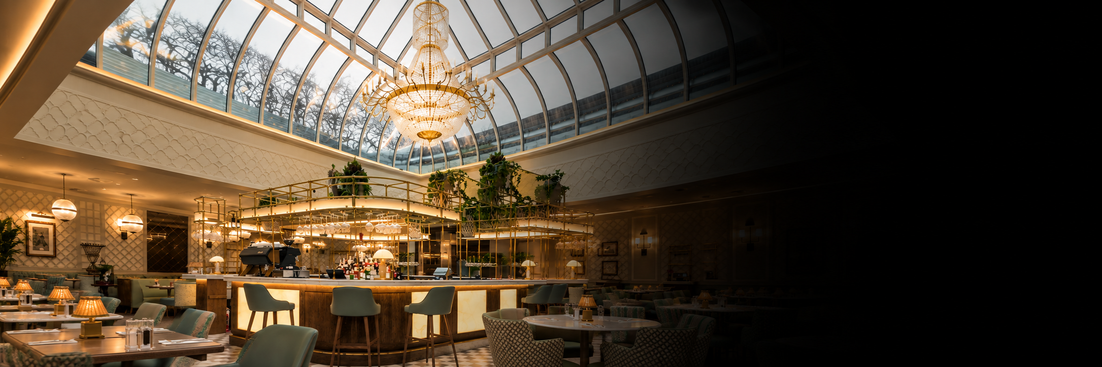 A wide interior view of a grand restaurant or bar with a large arched glass dome ceiling, hanging chandeliers, tables, chairs, and a bar counter. The right side is heavily darkened or obscured.
