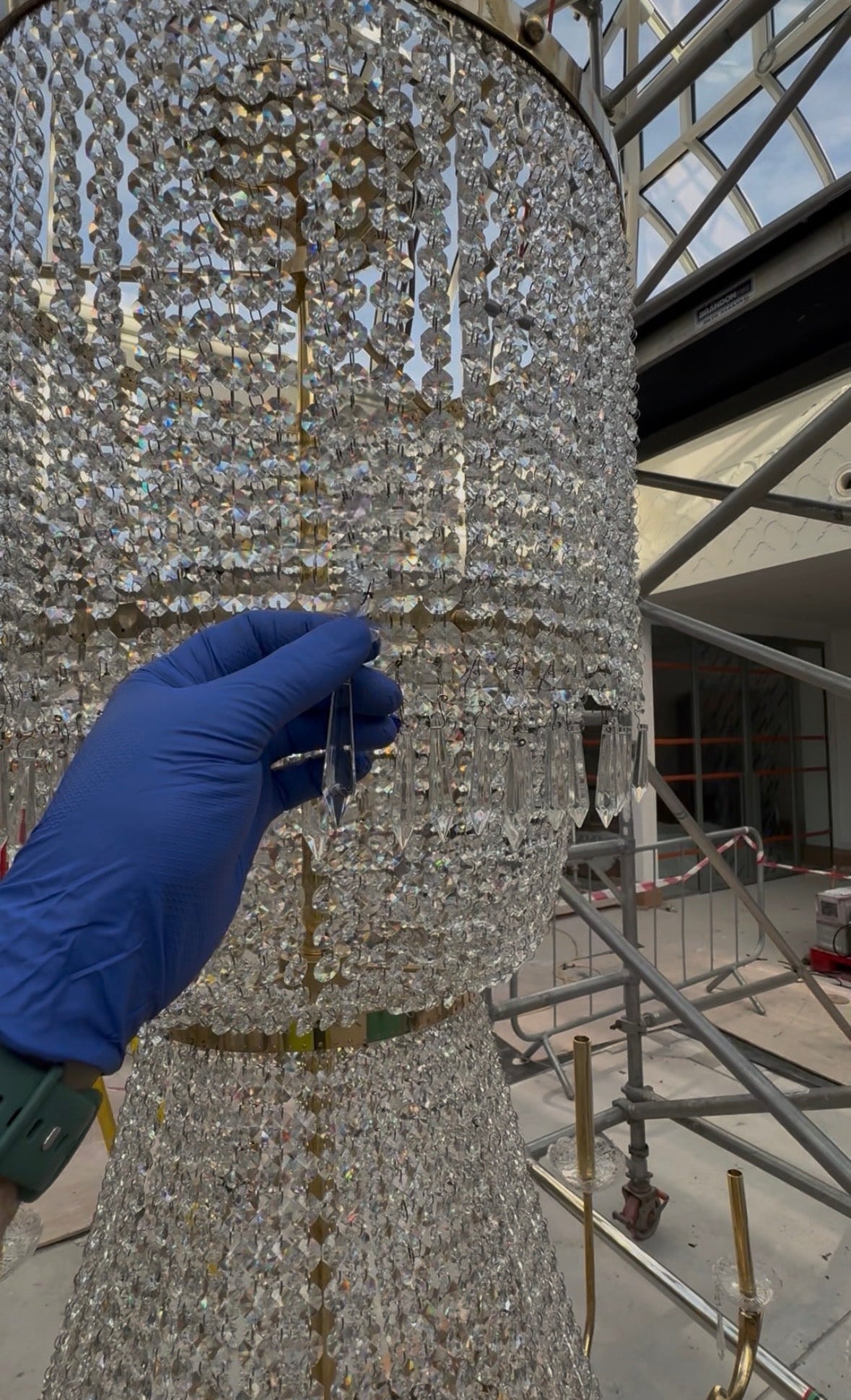 Hand wearing a blue glove touching a sparkling chandelier indoors.