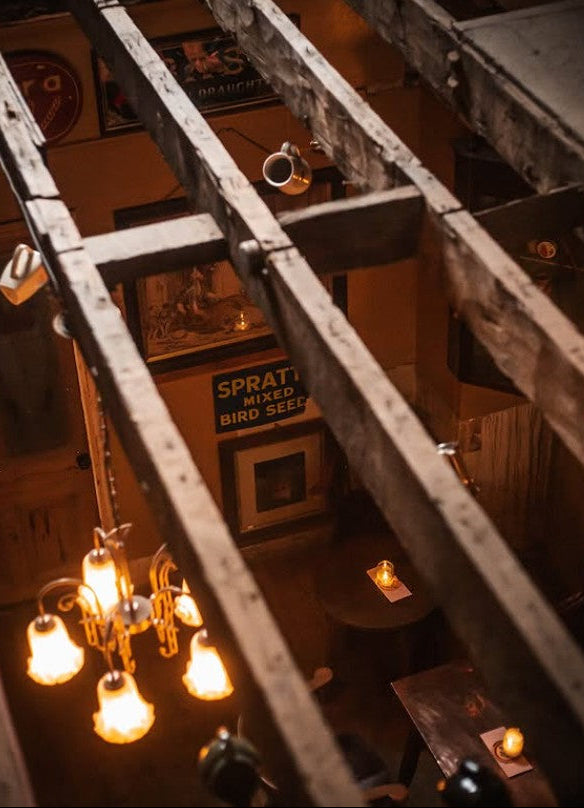 Indoors view of a cozy bar with wooden beams, chandelier, and warm lighting.
